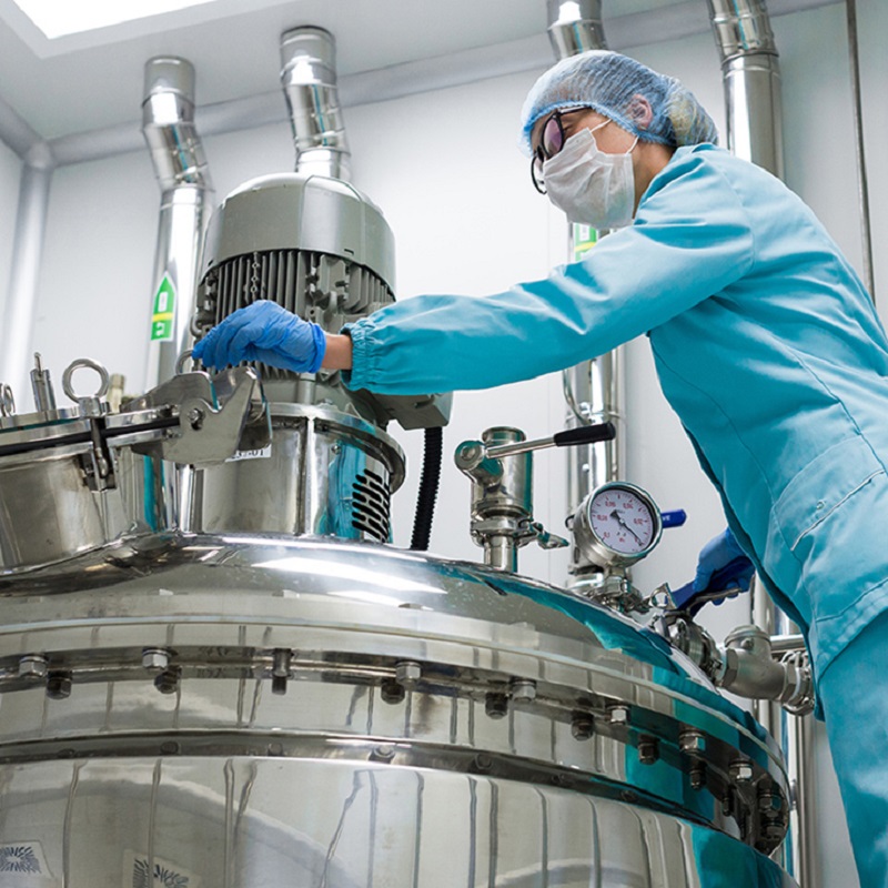 A factory worker in sterile clothing works with a large fermentation reactor.